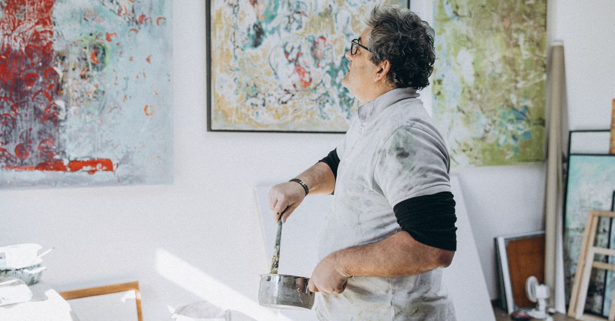 An artist painting on a canvas in a studio, surrounded by abstract artwork.